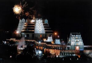 The illuminated ISKCON Sri Radha Krishna temple on Hare Krishna Hill in Bengaluru at night, with fireworks overhead
