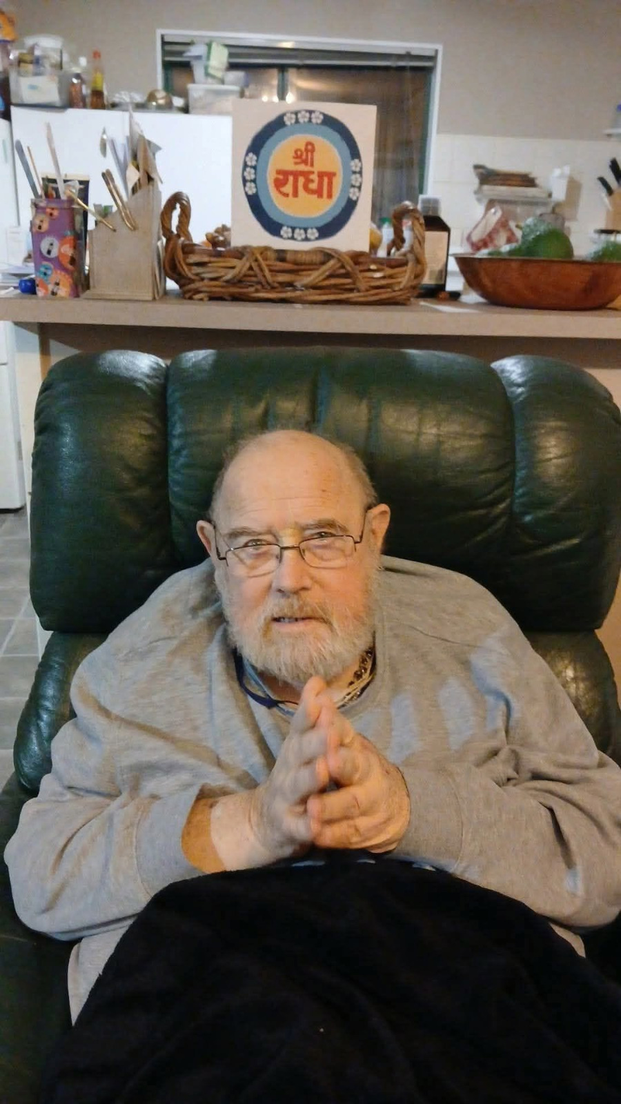 Jaya Tirtha Charan Dasa seated in an armchair at home in New Zealand, hands folded